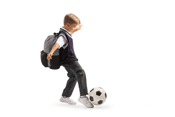 Full length profile shot of a schoolboy in a uniform kicking a soccer ball isolated on white background - Foto, Imagen