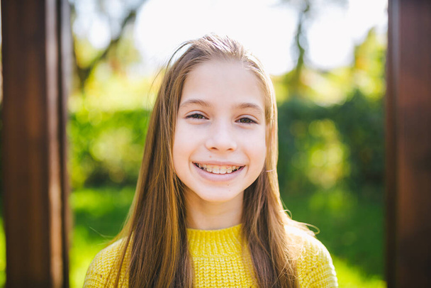 Retrato de adolescente feliz moderna con frenos dentales vestidos con ropa amarilla en el parque. Linda adolescente con frenos sonriendo alegremente. Niña en otoño sonriendo con aparatos de dientes ortopédicos. - Foto, Imagen
