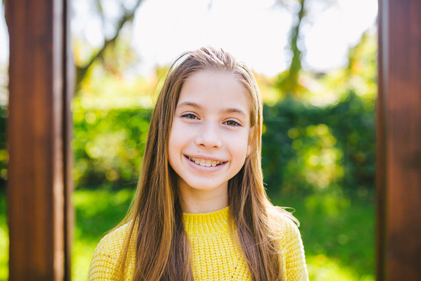 Portret van een modern gelukkig tienermeisje met gebitsbeugels gekleed in gele kleren in het park. Mooi tienermeisje met een vrolijk glimlachende beugel. Kid meisje in de herfst glimlachen met beugel tanden apparaat. - Foto, afbeelding