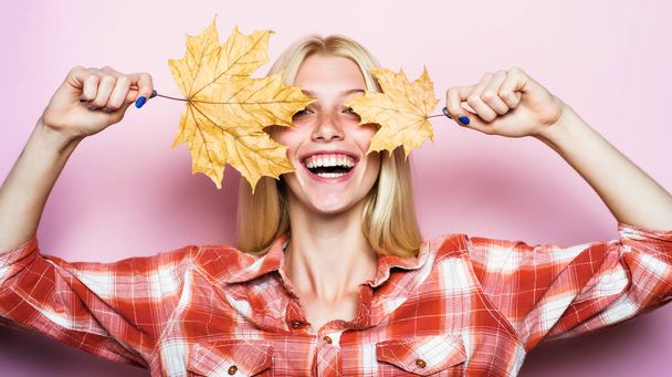 Jesienny nastrój. Uśmiechnięta Dziewczyna przykryła oczy liściem klonu. Jesienna moda. Szczęśliwa kobieta ze złotymi liśćmi. - Zdjęcie, obraz