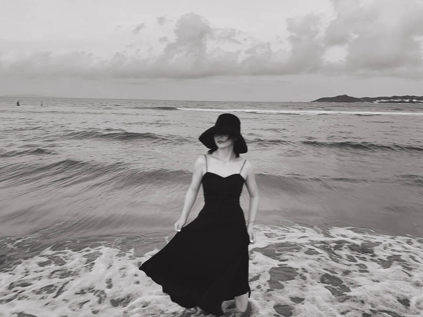 beautiful young woman in black dress walking on the beach - Фото, изображение
