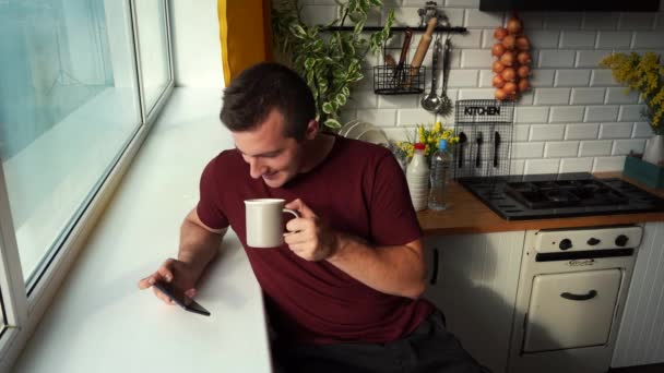 Mann trinkt Tee am Morgen und schaut gleichzeitig Nachrichten am Telefon - Filmmaterial, Video