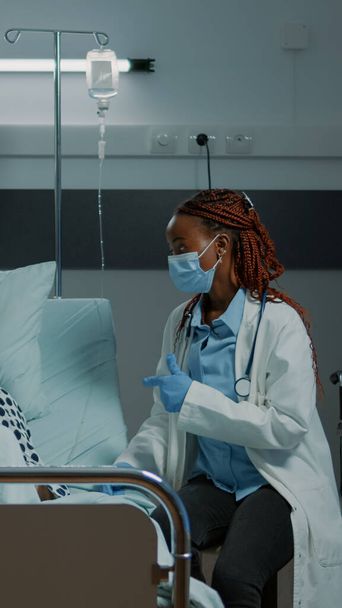 Afro-Amerikalı doktor hastane koğuşunda hasta bir hastayla konuşuyor. - Fotoğraf, Görsel