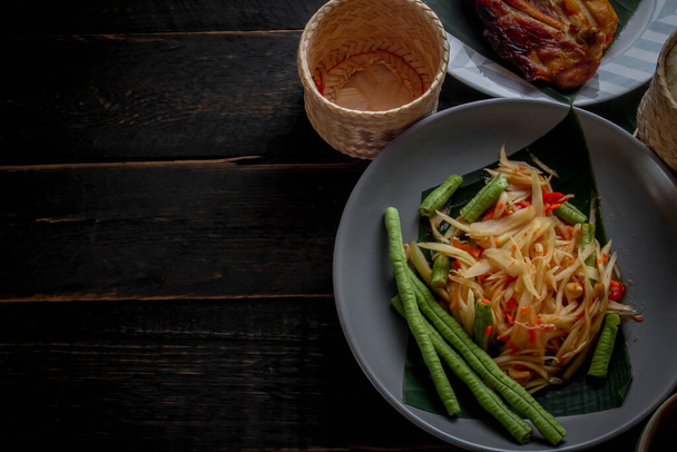 タイ料理はタイとアジアの両方で、「パパヤサラダ」または私たちが呼ぶように、「ソムタム」は焼きチキンともち米と新鮮な炒め物で補完されています。黒の木製のテーブルの上で提供. - 写真・画像