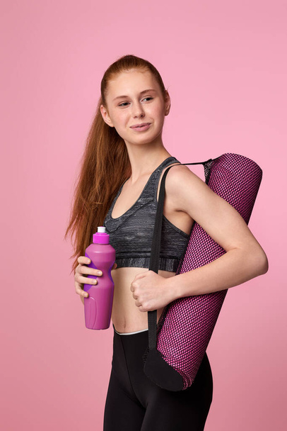 woman in sportswear holding bottle of water and fitness mat - Foto, Bild