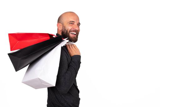 Happy young man with beard carries shopping bags over shoulder on white background. Horizontal banner image. Copy space. - Foto, afbeelding