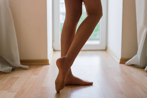Piernas desnudas femeninas, permaneciendo de puntillas, piel sana y lisa, haciendo ejercicio por la mañana en la ventana. De cerca. - Foto, imagen