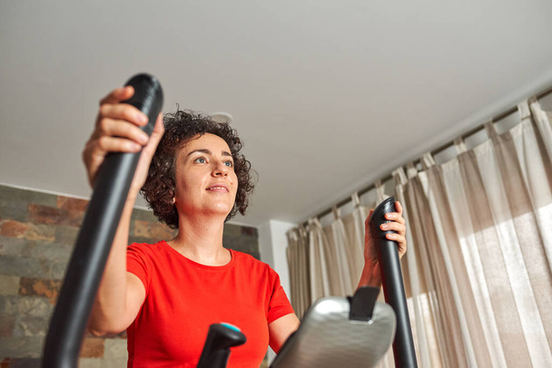 Entrenamiento de fitness para mujer en casa con un entrenador elíptico inteligente en interiores - Foto, imagen