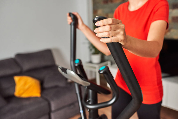 Unrecognizable woman at home training on smart elliptical trainer indoors in daylight with natural light - Photo, Image