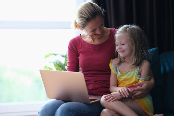 Sorridente mamma e figlia seduta sul divano e guardando il computer portatile - Foto, immagini