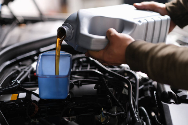 Locksmith mechanic pours engine oil into plastic container on motor engine - Photo, Image