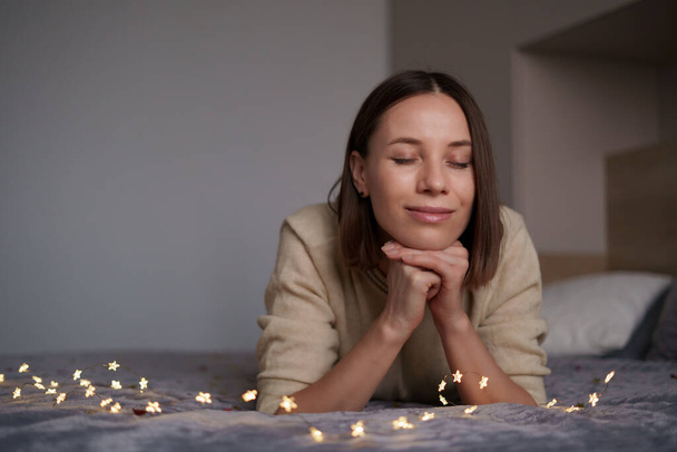 Schöne Frau liegt mit leuchtenden Lichtern auf dem Bett - Foto, Bild