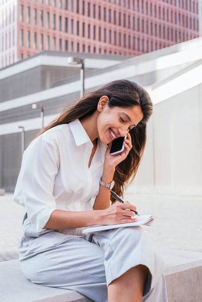 young indian female lawyer taking notes while talking by phone - Photo, Image