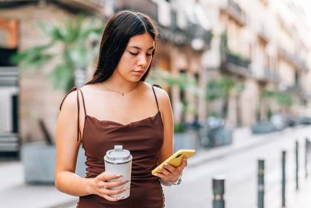 young asian woman holding a reusable take away coffee mug and using her phone - Foto, immagini