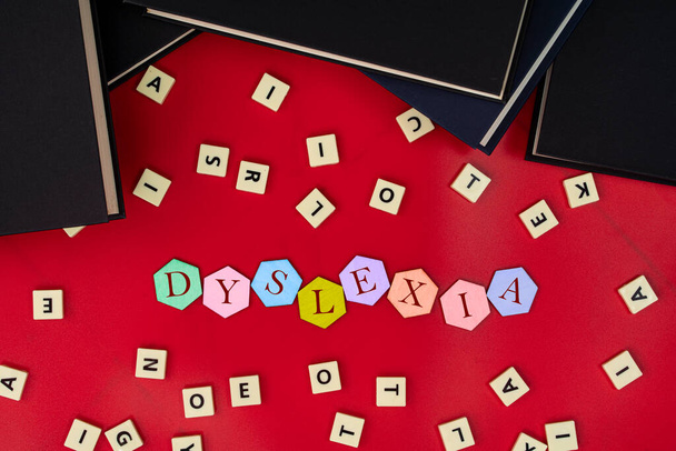 Baldosas hexagonales con letras que deletrean DYSLEXIA con baldosas y libros de plástico. La dislexia es un trastorno de la lectura. Concepto de aprendizaje - Foto, imagen