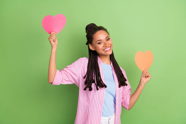 Photo of funky sweet dark skin lady wear pink shirt smiling holding two hearts dancing isolated green color background - Фото, изображение