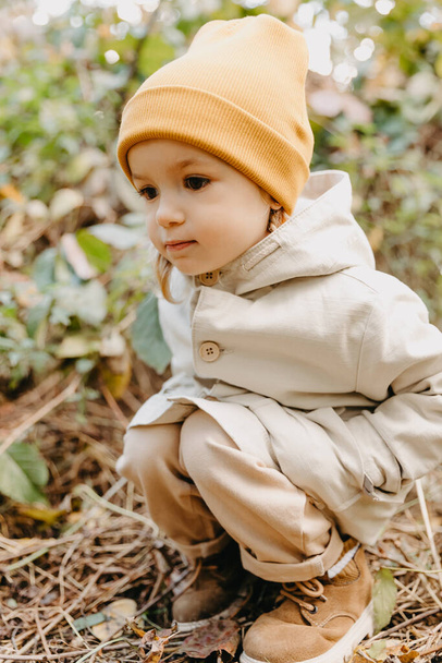 portrait of a child dressed in a stylish spring raincoat and a yellow hat. Happy and cheerful baby on a walk  - Foto, Imagen