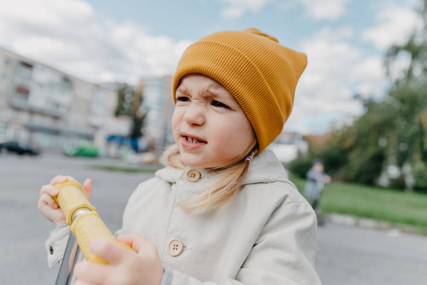 portrait of a child dressed in a stylish spring raincoat and a yellow hat. Happy and cheerful baby on a walk  - Foto, Imagen