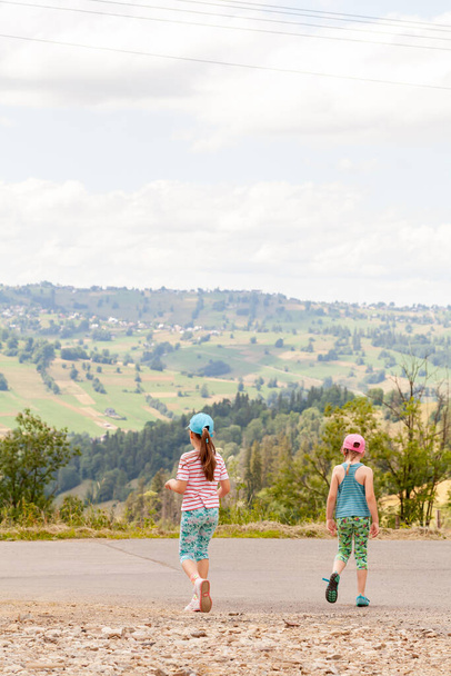 Két fiatal elemi korú gyermek utazik, kislányok, nővérek felfedezik együtt, séta az úton, dombok, festői hegyvidéki terület, vidéki nyári szünidő, nyaralás. Európa, Lengyelország - Fotó, kép