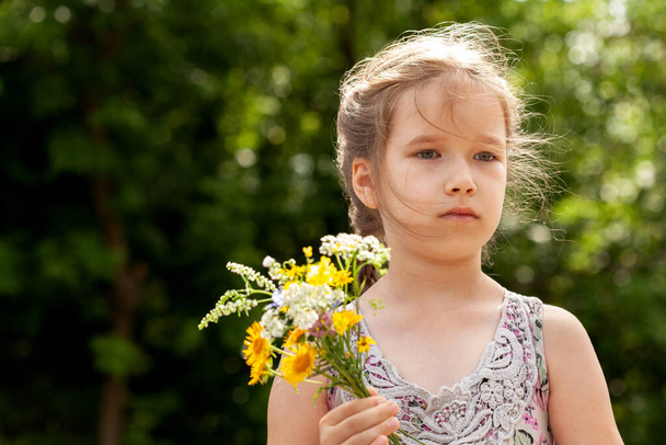 Okul çağındaki çocuk, küçük ilkokul çocuğu elinde bir buket ot ve kır çiçeği tutan küçük kız, yaz portresi, yüz kaplaması, bir kişi. Boşluğu, bulanık arkaplanı, çocukları ve doğayı kopyala - Fotoğraf, Görsel