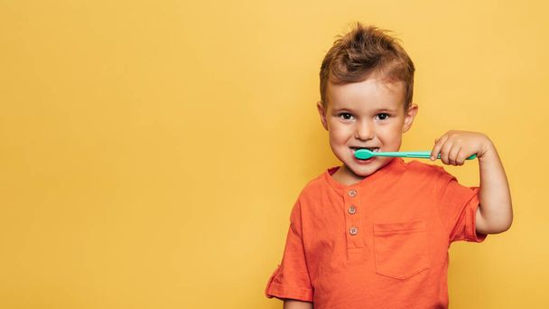 Boldog kisbaba fiú, aki fogat mos egy sárga hátterű fogkefével. Egészségügy, szájhigiénia. Egy hely az üzenetednek.. - Fotó, kép