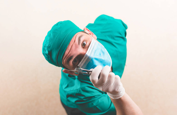 Fiatal orvos zöld sebész ruha és védő légzőmaszk lándzsával a kezében izolált a sárga háttér - Fotó, kép