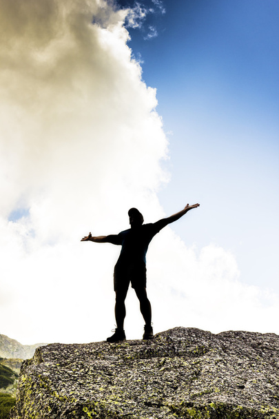 Άτομο που στέκεται στην κορυφή ενός βράχου, με τα χέρια υψωμένα - Φωτογραφία, εικόνα