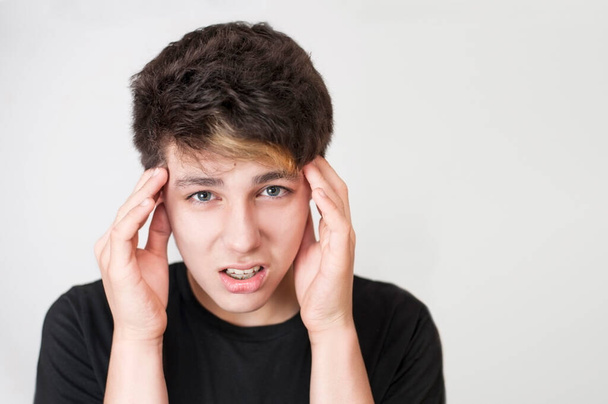A boy of adolescence holds his head and is sorry for having a headache because he has braces on his lower jaw. Copy space - Foto, Imagem