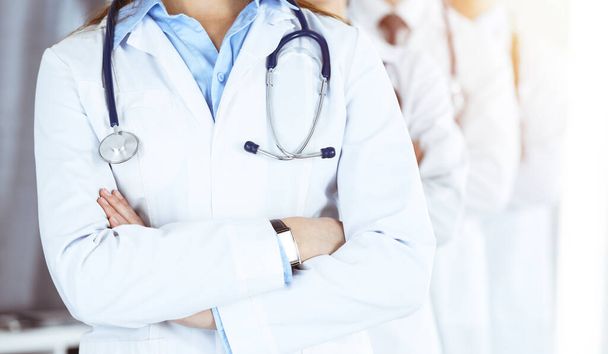 Group of modern doctors standing as a team with arms crossed in sunny hospital. Medical help, insurance in health care, best desease treatment and medicine concept - Photo, Image