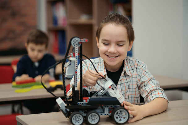 Два мальчика разных возрастов играют с игрушками-роботами в школе на уроке робототехники - Фото, изображение