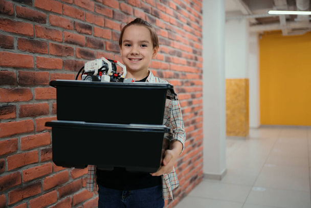 Chlapec chůze při držení krabic robotické pokoje na cihlové zdi pozadí - Fotografie, Obrázek