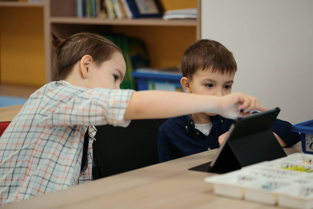 İki farklı yaşta çocuk okul robotları sınıfında robot oyuncaklarla oynuyor. - Fotoğraf, Görsel
