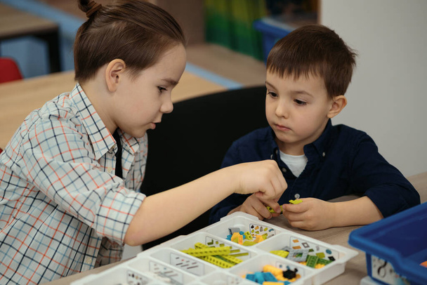 Dos niños niños de diferentes edades jugando con un juguete robot en la clase de robótica escolar - Foto, imagen