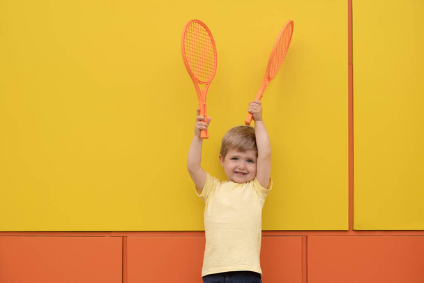 Sarı duvarda tenis raketi olan bir çocuk. - Fotoğraf, Görsel
