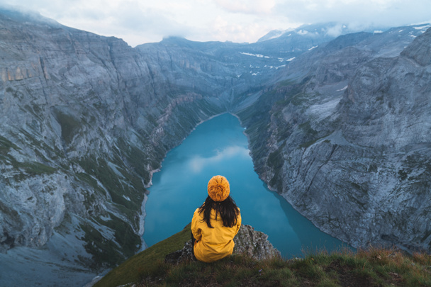 Vue arrière de la jeune femme en veste jaune debout sur le sommet de la montagne et regardant le lac Limmernsee. Femme assise au bord de la montagne et profitant de la belle vue à Glarus, Suisse - Photo, image