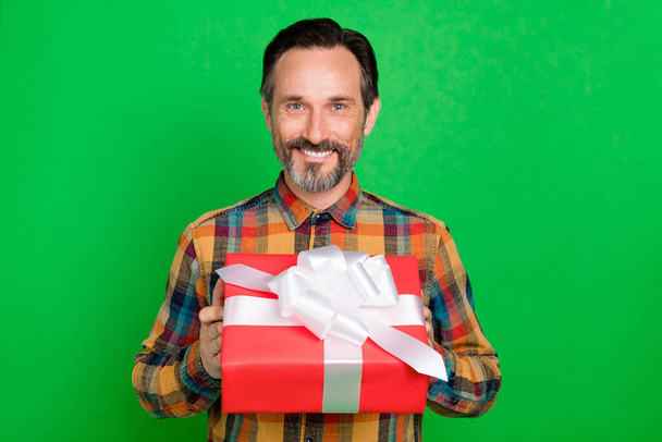 Porträt eines attraktiven, fröhlichen Mannes mit einem Geschenk in der Hand, das Sie isoliert über hellgrünem Hintergrund erscheinen lässt - Foto, Bild