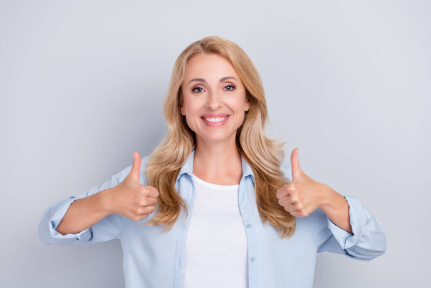 Photo of positive nice lady raise two thumbs up agree toothy smile wear blue shirt isolated grey color background - Foto, immagini