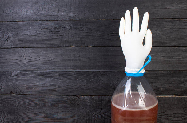 The production of wine. A plastic bottle with a young homemade wine and put on the neck of a rubber glove for fermentation. On a black wooden background. - Foto, Imagem