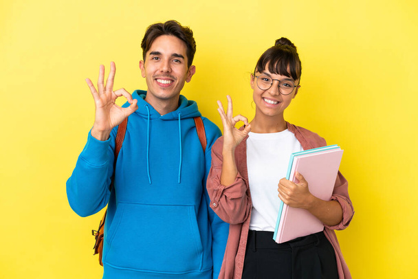 Jeune couple étudiant isolé sur fond jaune montrant un signe ok avec les doigts - Photo, image