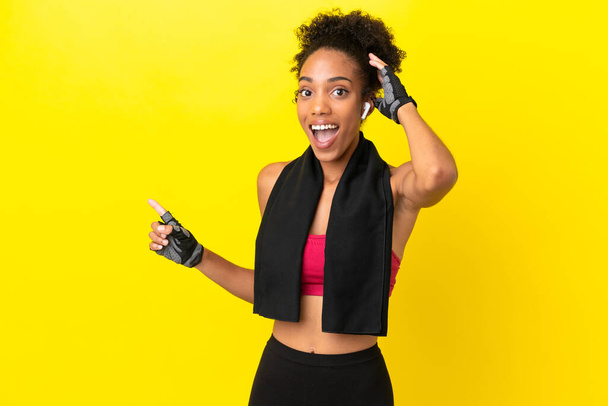Young African sport woman isolated on yellow background surprised and pointing finger to the side - Photo, Image
