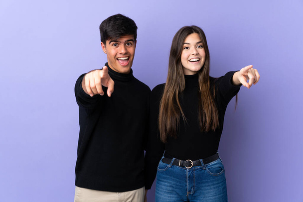 Young couple over isolated purple background points finger to the front - Photo, Image