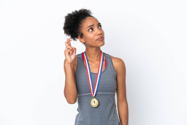 Молодая афроамериканка с медалями изолированы на белом фоне с пальцами скрещивания и желающих лучшего - Фото, изображение