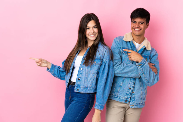 Junges Paar auf isoliertem rosa Hintergrund zeigt mit dem Finger zur Seite in Seitenlage - Foto, Bild