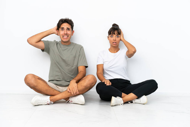 Jeune couple mixte assis sur le sol isolé sur fond blanc prend les mains sur la tête parce que a migraine - Photo, image
