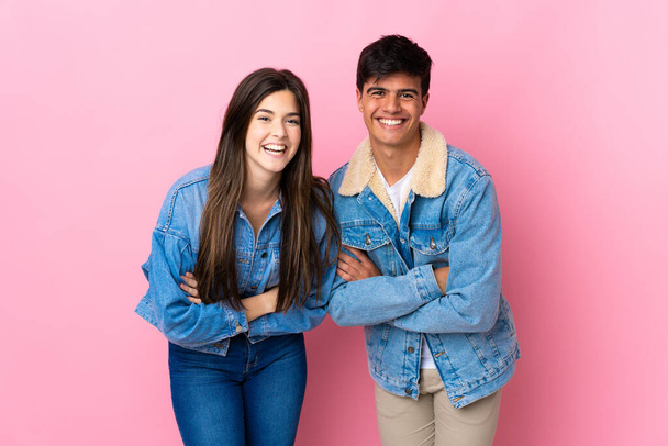 Молодая пара на изолированном розовом фоне держит руки скрещенными, улыбаясь - Фото, изображение