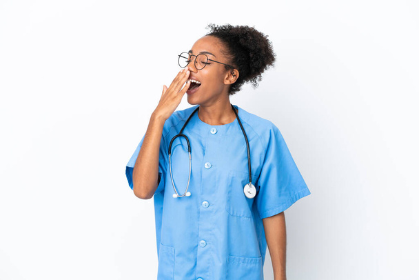 Jeune chirurgien afro-américaine médecin femme isolée sur fond blanc bâillant et couvrant la bouche grande ouverte avec la main - Photo, image
