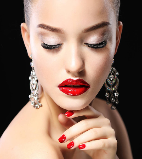 Portrait of young beautiful woman with evening make up touching her face over black background. Red lips and nails. - Photo, Image