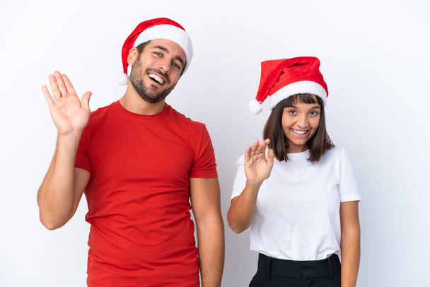 Noel şapkalı genç çift beyaz arka planda izole edilmiş mutlu bir ifadeyle selamlıyorlar. - Fotoğraf, Görsel