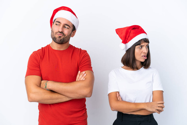 Молодая пара в рождественской шляпе изолированы на белом фоне с запутанным выражением лица в то время как кусает губы - Фото, изображение