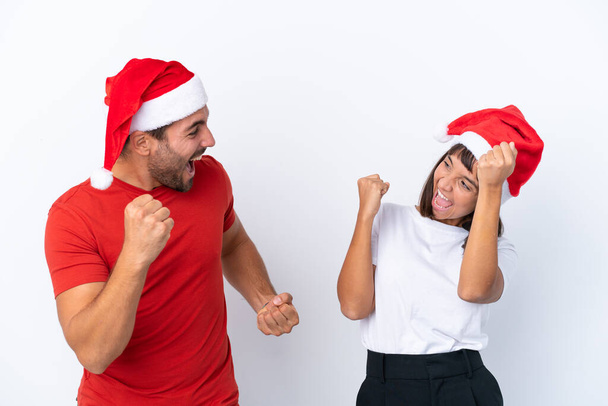 Νεαρό ζευγάρι με χριστουγεννιάτικο καπέλο απομονώνονται σε λευκό φόντο γιορτάζει μια νίκη στη θέση του νικητή - Φωτογραφία, εικόνα